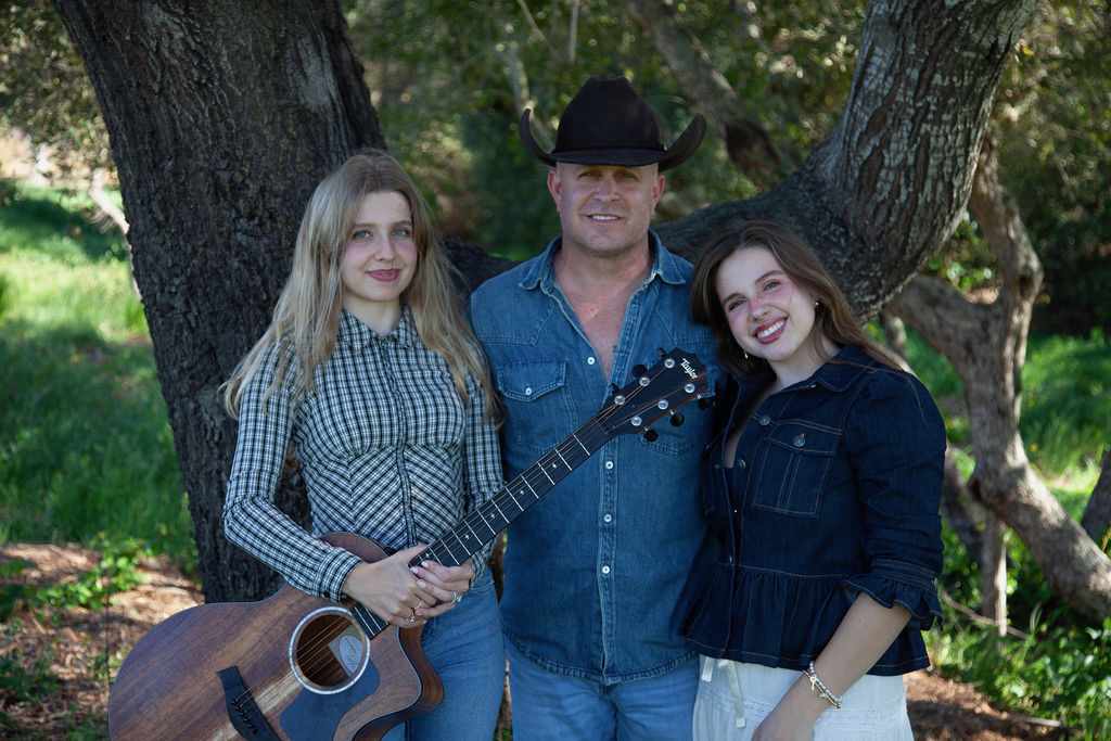 Three Rowdy Band members photographed outdoors with an acoustic guitar