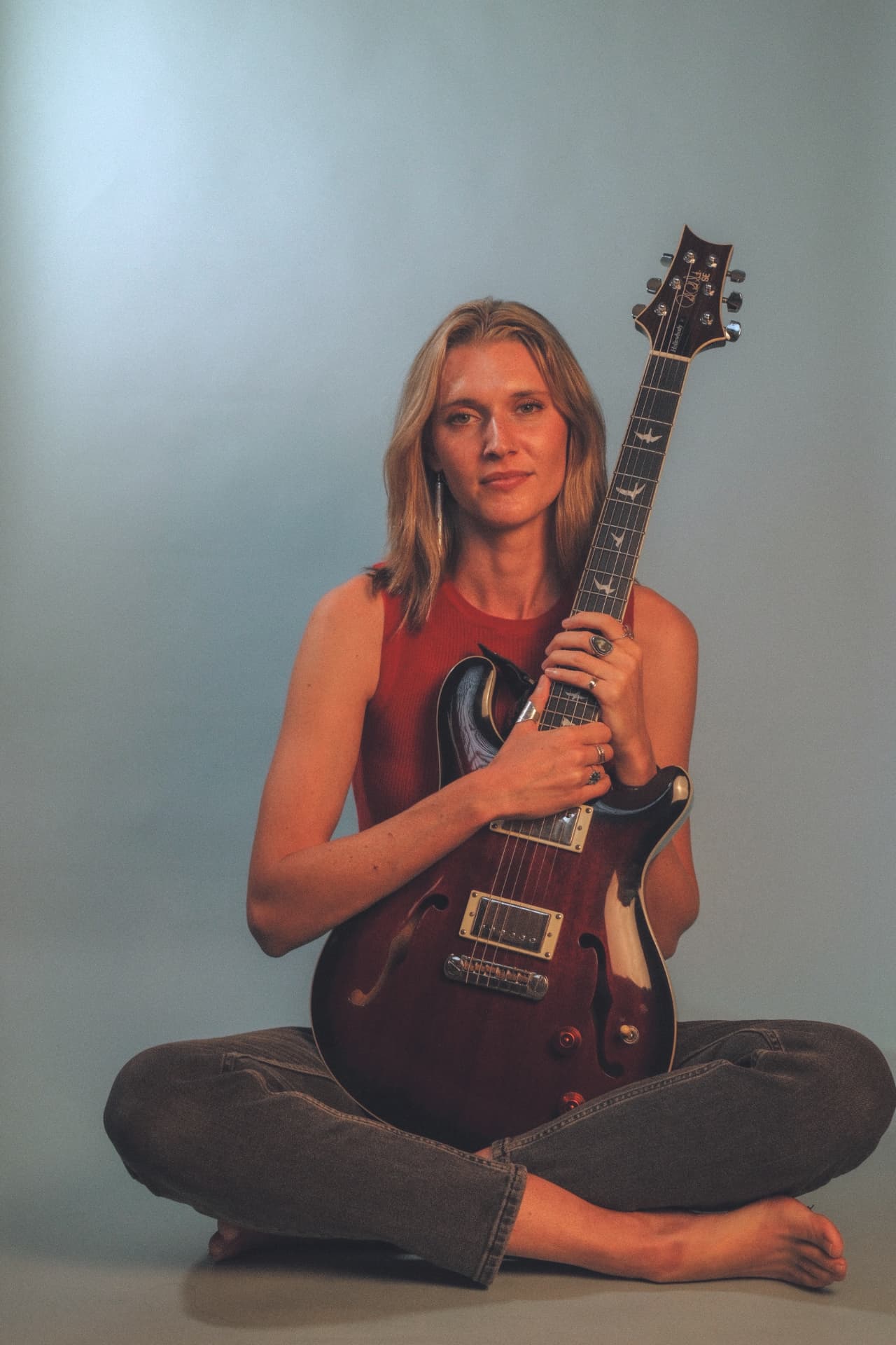 Anna Ballew seated cross-legged holding her guitar